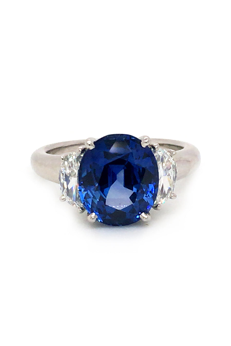Platinum ring with oval blue sapphire and two half-moon diamonds on white background