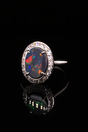 Angle of 18K white gold ring with a black opal surrounded with brilliant diamonds on a black background.