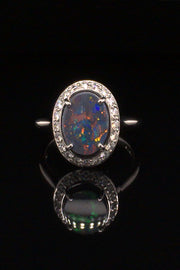 18K white gold ring with a black opal surrounded with brilliant diamonds on a black background.
