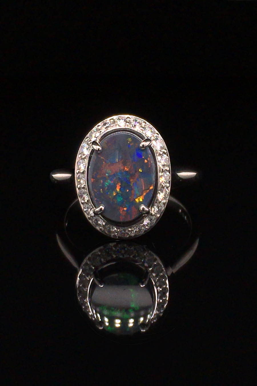 18K white gold ring with a black opal surrounded with brilliant diamonds on a black background.