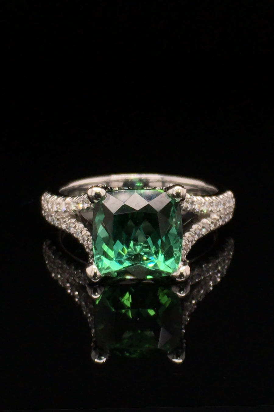 18K white gold ring with a cushion green tourmaline and diamonds on a black background.
