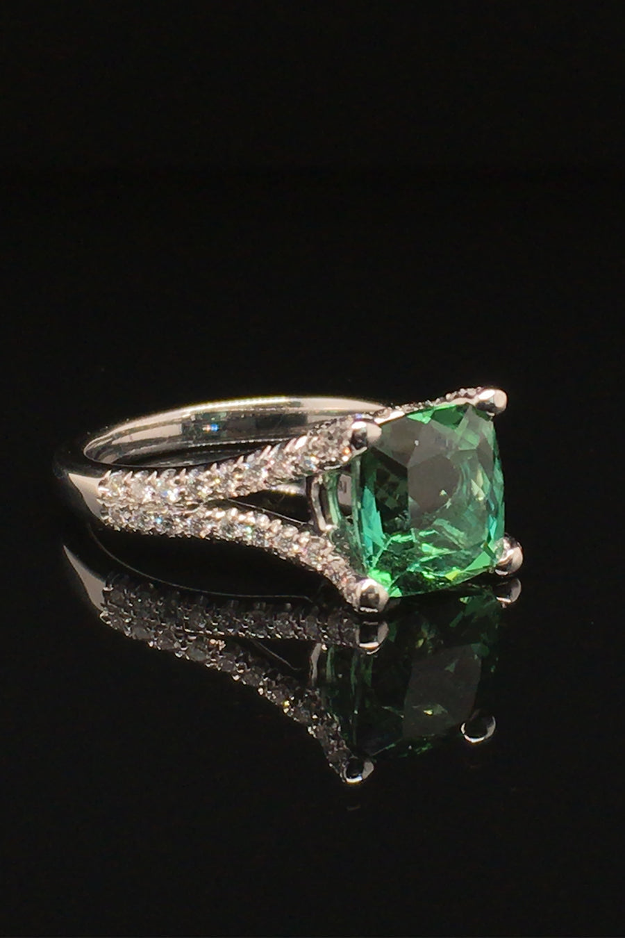 Side view of 18K white gold ring with a cushion green tourmaline and diamonds on a black background.
