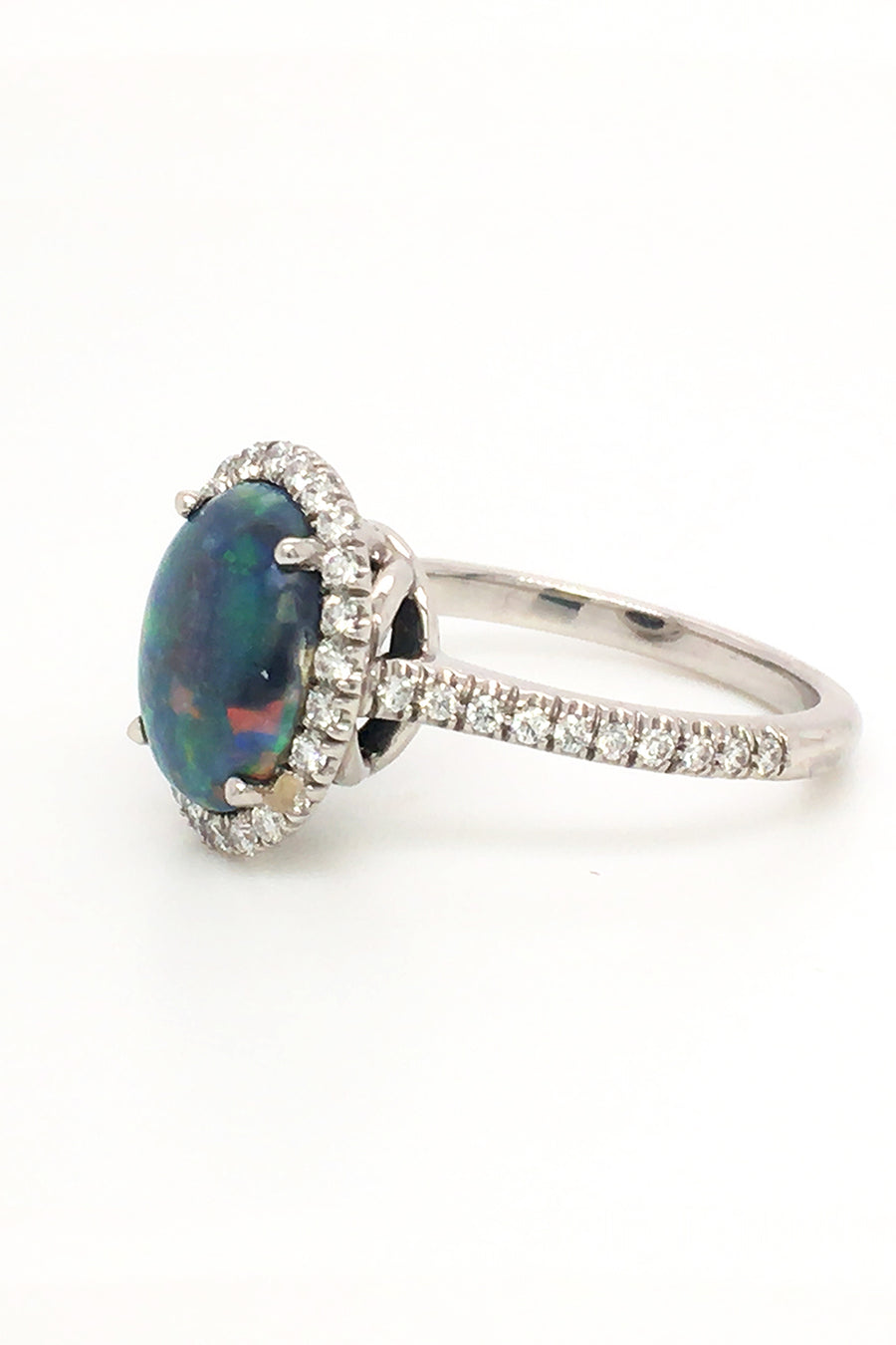 Side view of platinum ring with a black opal and diamonds on a white background