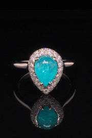 Platinum ring with a pear-shape Brazilian paraiba cabochon and pave diamonds on black background.