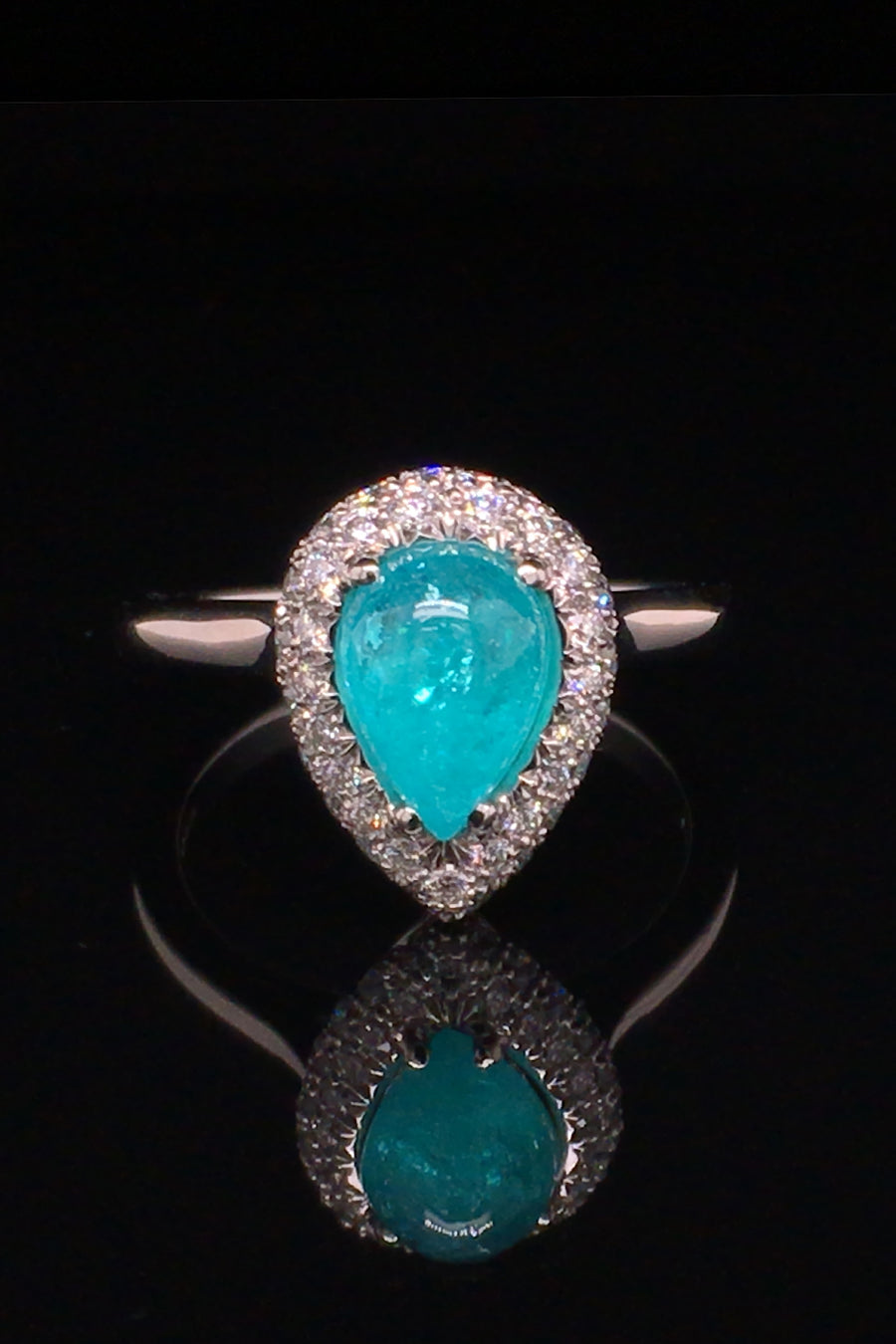 Platinum ring with a pear-shape Brazilian paraiba cabochon and pave diamonds on black background.