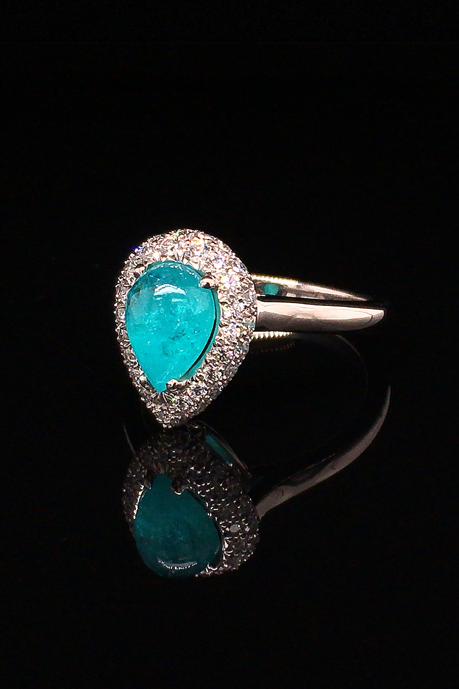 Angle view of a platinum ring with a pear-shape Brazilian paraiba cabochon and pave diamonds on black background.