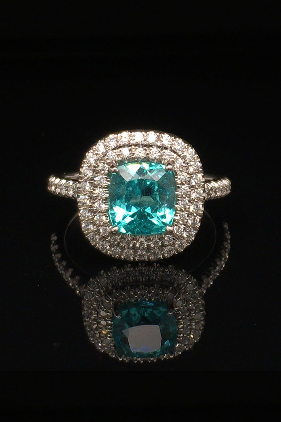 Platinum ring with a cushion-cut African paraiba with a double halo of brilliant diamonds on a black background.