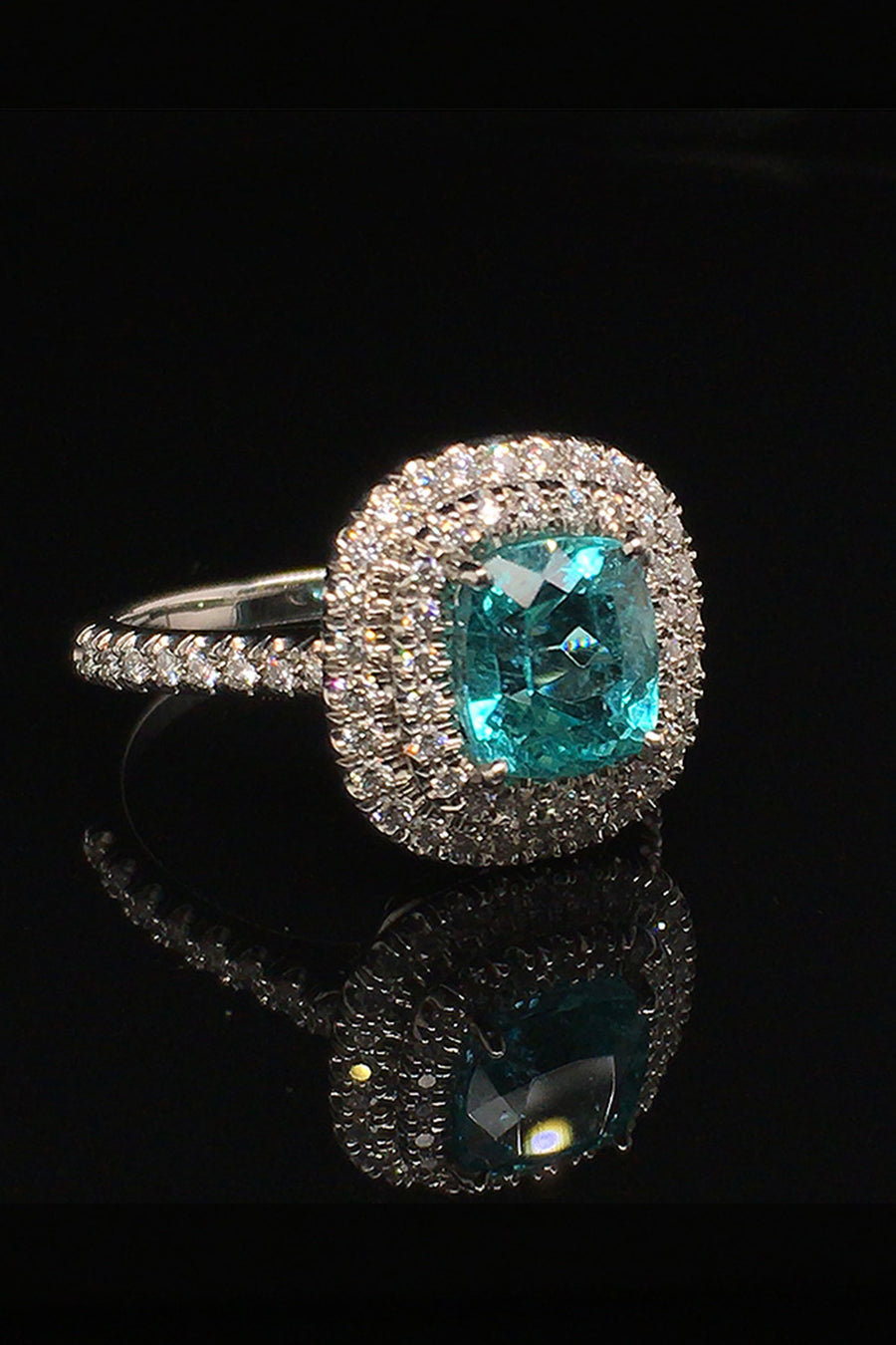Angle view of platinum ring with a cushion-cut African paraiba with a double halo of brilliant diamonds on a black background.