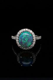 Platinum ring with a black opal and diamond halo on a black background.