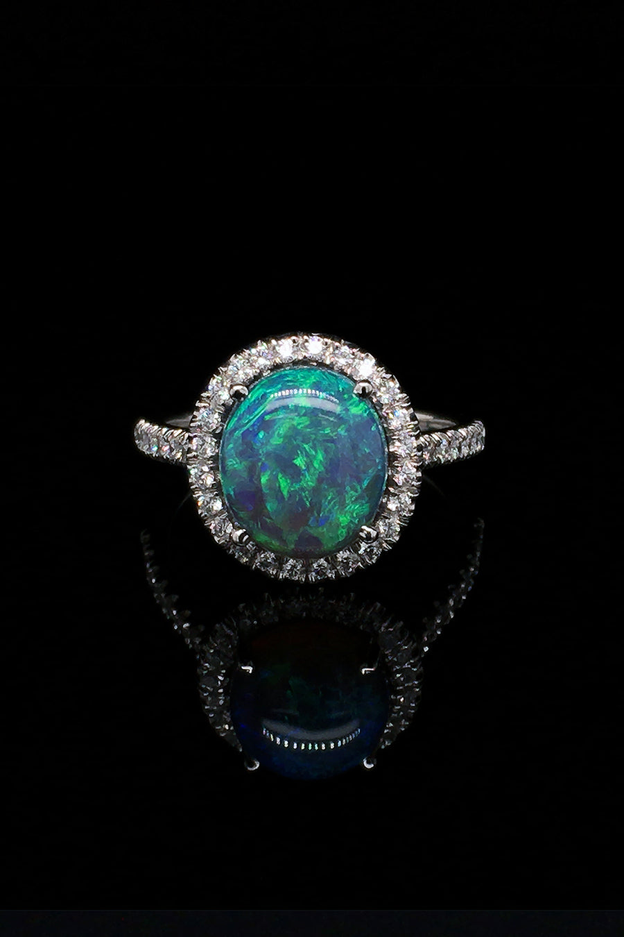 Platinum ring with a black opal and diamond halo on a black background.