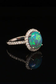 Angle view of platinum ring with a black opal and diamond halo on a black background.