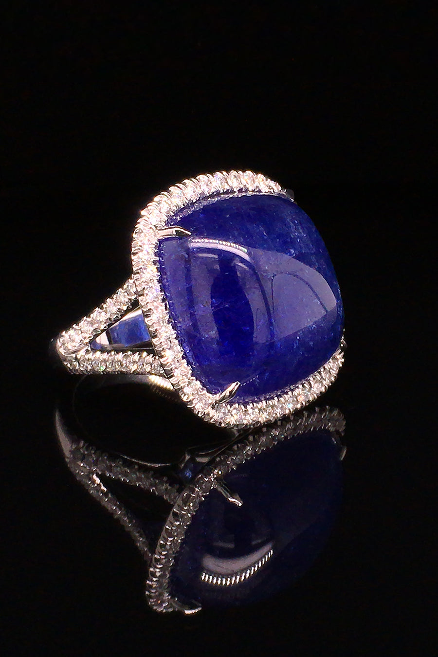Angle view of 18K white gold ring with a cushion cabochon tanzanite with a diamond halo on a black background