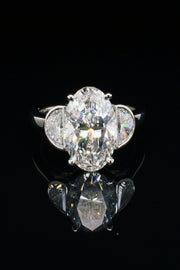 A platinum ring with oval diamond center and two half moon stones on a black background.