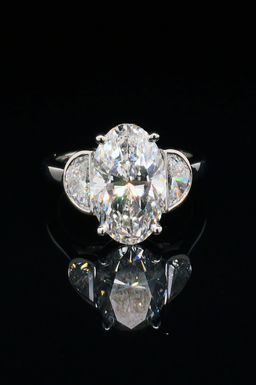 A platinum ring with oval diamond center and two half moon stones on a black background.
