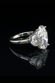 Side view platinum ring with oval diamond center and two half moon stones on a black background.