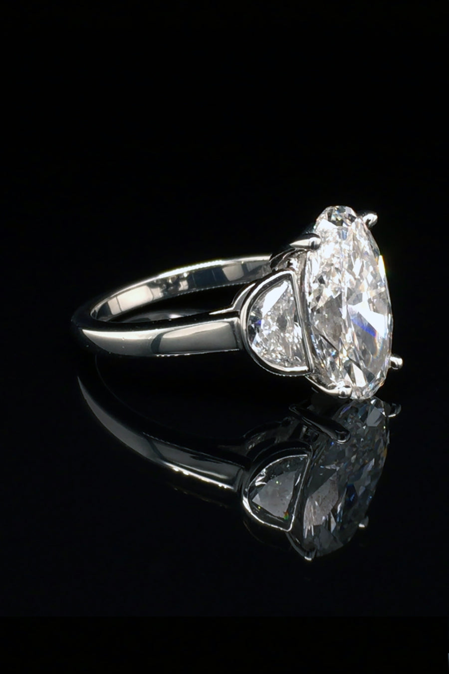 Side view platinum ring with oval diamond center and two half moon stones on a black background.