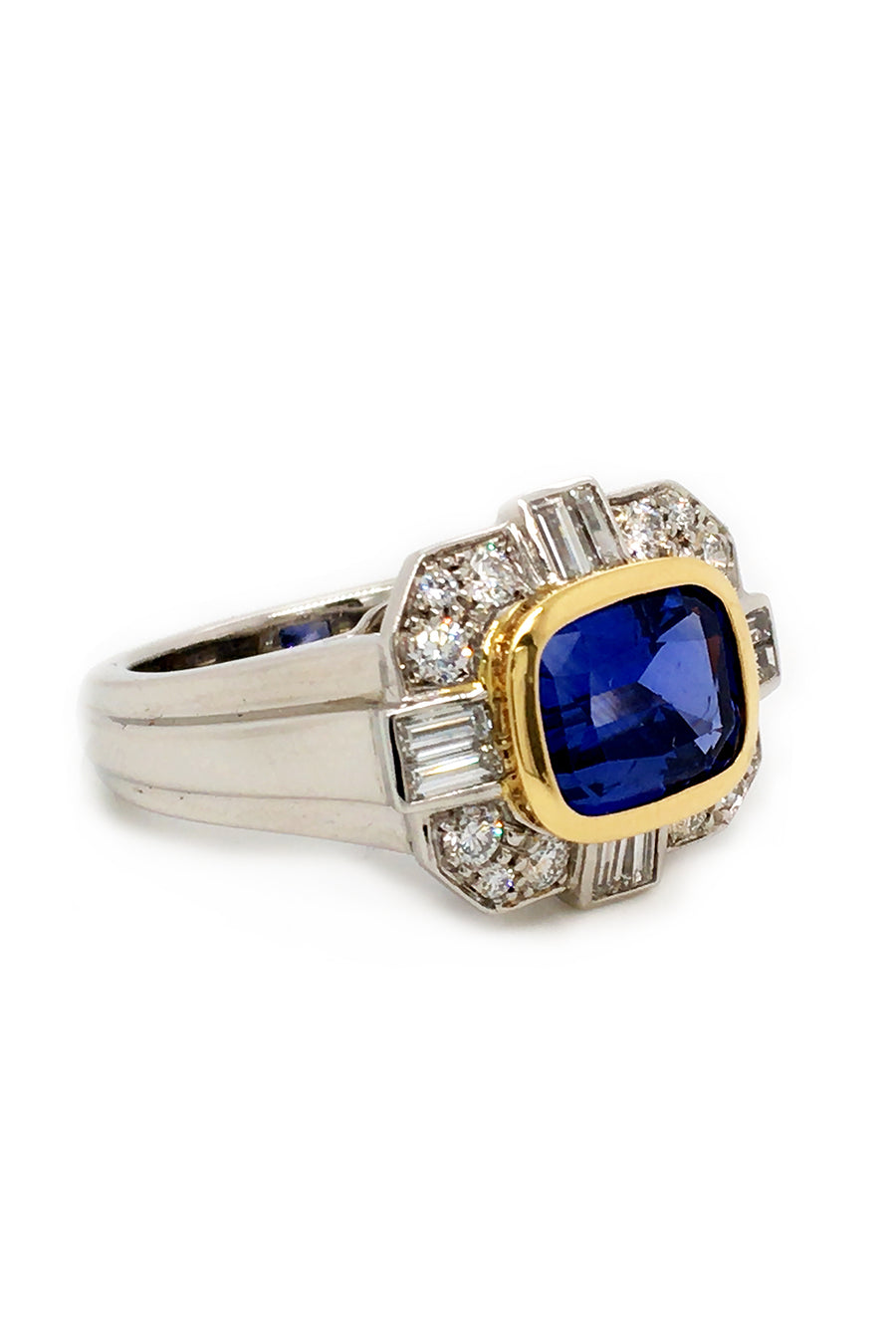 Angle view of ring with a blue sapphire in 18K yellow gold with baguettes and brilliant diamonds set in platinum on a white background