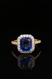 Emerald-cut sapphire set in platinum and surrounded by diamonds with an 18K yellow gold band with diamonds on a black background.
