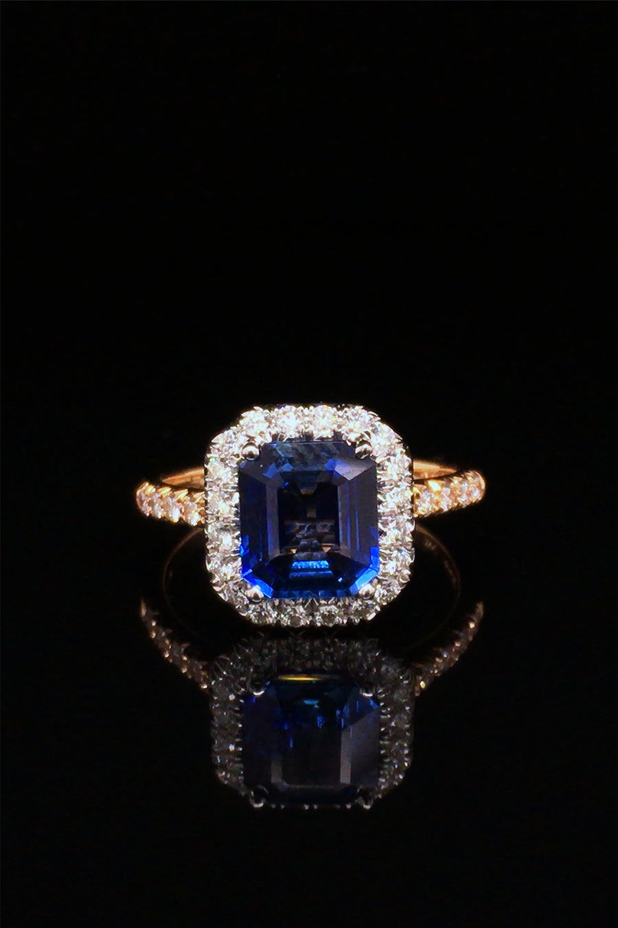 Emerald-cut sapphire set in platinum and surrounded by diamonds with an 18K yellow gold band with diamonds on a black background.