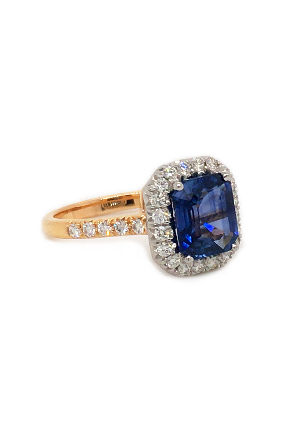 Angle view of emerald-cut sapphire set in platinum and surrounded by diamonds with an 18K yellow gold band with diamonds on a white background.
