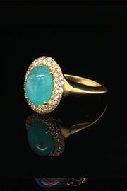 Angle view of 18K yellow gold ring with oval Brazilian paraiba cabochon and pave diamond halo on a black background.