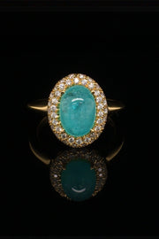 18K yellow gold ring with oval Brazilian paraiba cabochon and pave diamond halo on a black background.