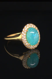 Angle view of 18K yellow gold ring with oval Brazilian paraiba cabochon and pave diamond halo on a black background.