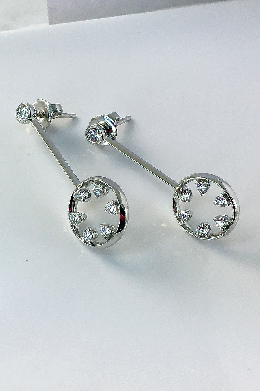 Side view of 18K white gold and diamond drop earrings featuring circle motif on a white background