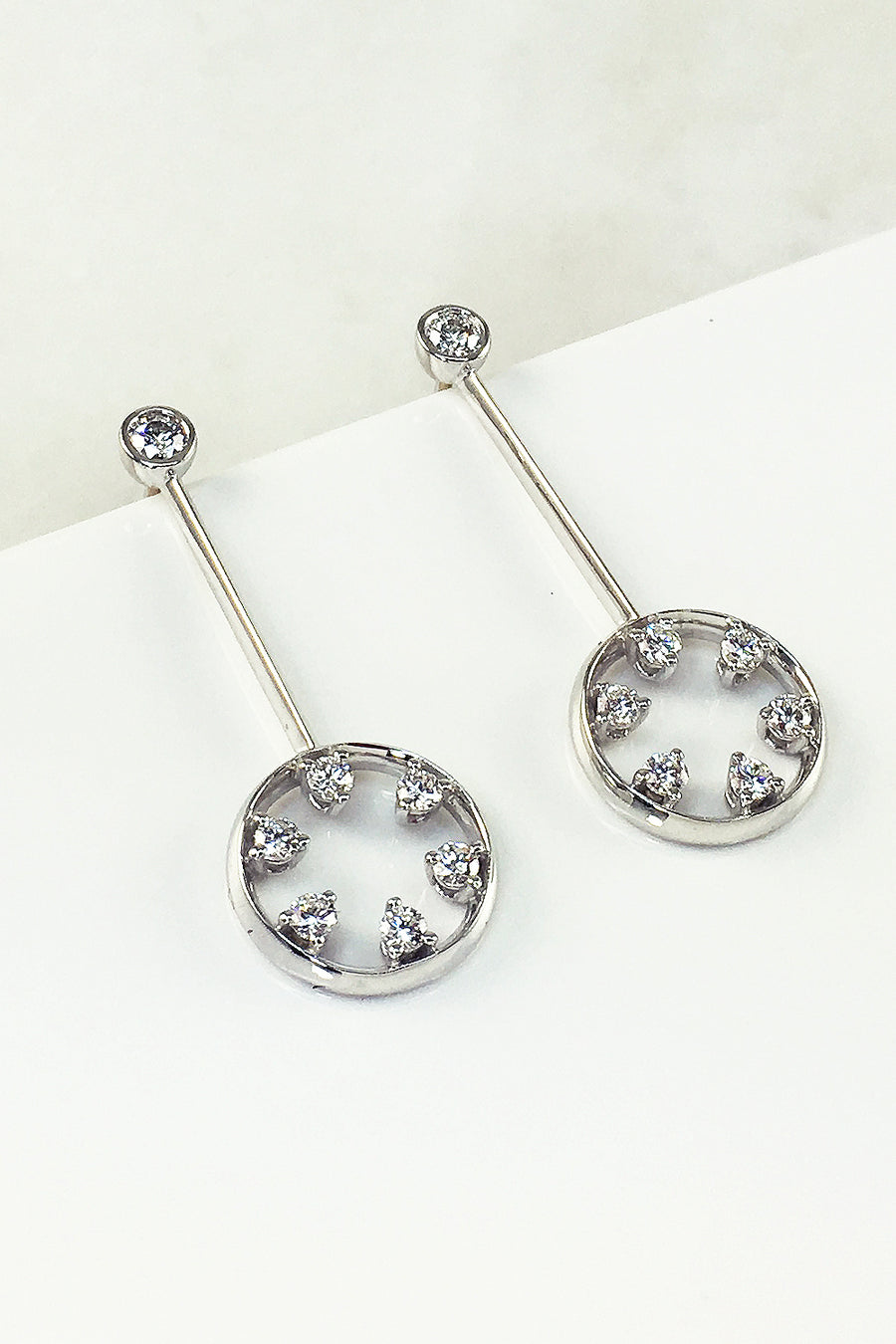 18K white gold and diamond drop earrings featuring circle motif on a white background