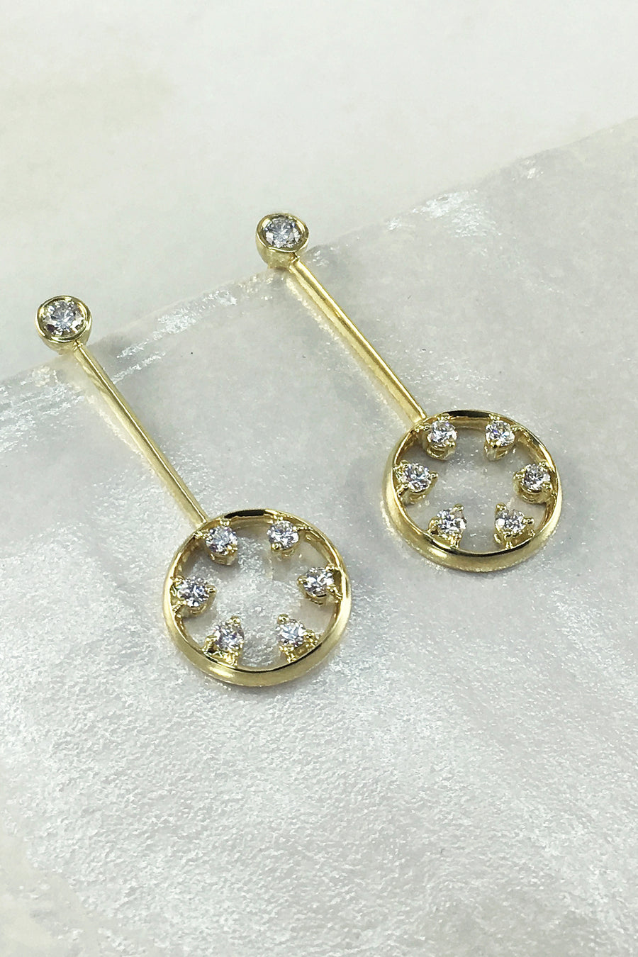18K yellow gold and diamond drop earrings featuring circle motif on a textured white surface