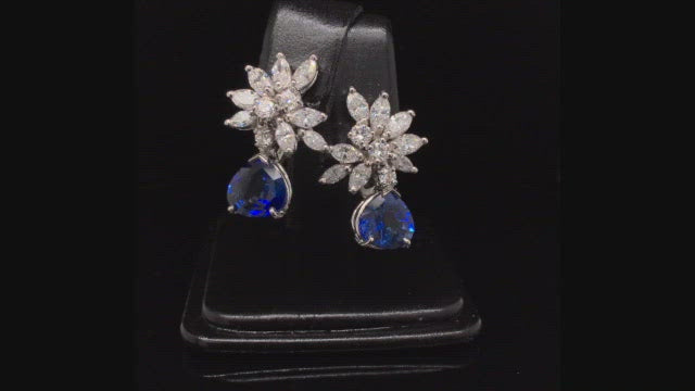 Video of rotating platinum earrings with a diamond cluster with pear-shape sapphire drops on black background