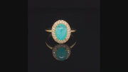 Video of rotating 18K yellow gold ring with oval Brazilian paraiba cabochon and pave diamond halo on a black background.